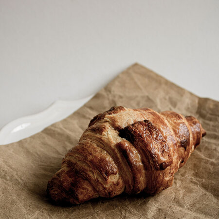Ein einzelnes Croissant liegt auf einem braunen Papier auf einem weißen Teller