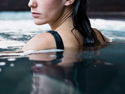 Frau mit nassem schwarzen Badeanzug steht im Wasser und blickt seitlich weg