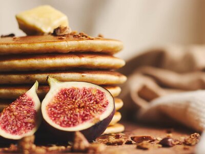 Nahaufnahme eines Stapels Pfannkuchen mit Butter obenauf und zwei halbierten Feigen davor