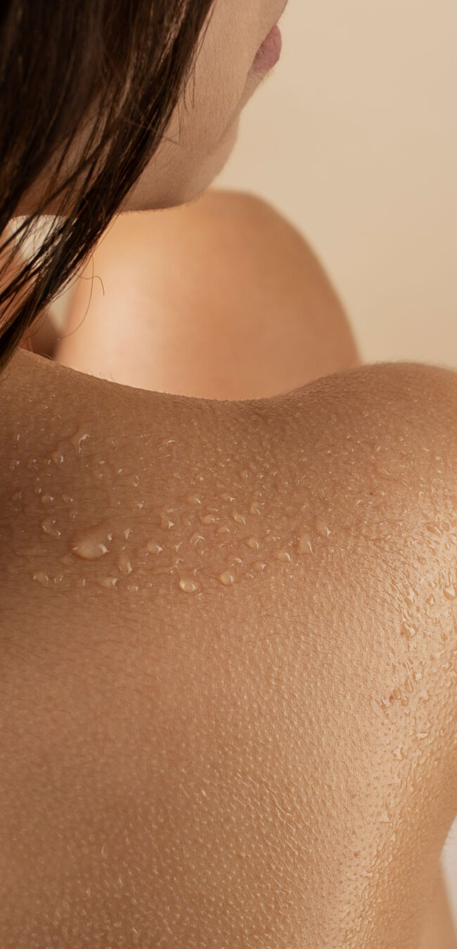 Nahaufnahme einer weiblichen Schulter mit Wassertropfen und seitlich sichtbarem Haar