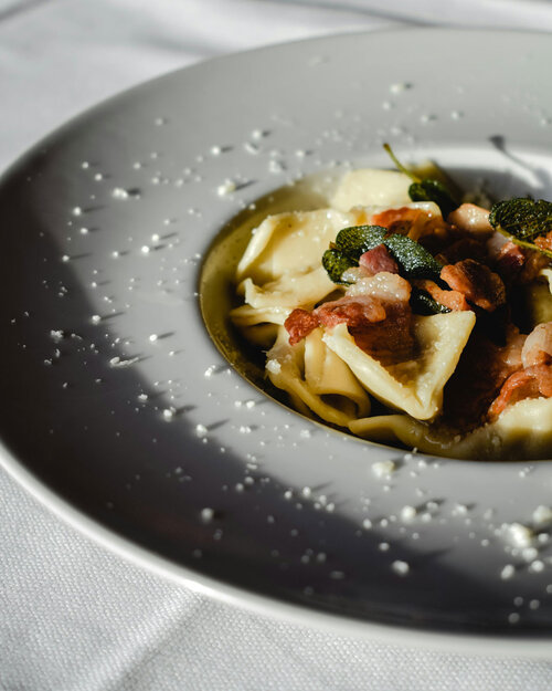 Nahaufnahme eines weißen Tellers mit Pasta, Speckstücken und Salbeiblättern