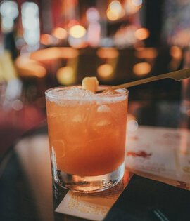 Glas mit Cocktail, das mit einem Holzstäbchen garniert wird