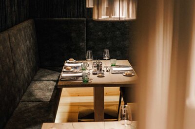 Gedeckter Esstisch mit Gläsern, Tellern und Besteck an einer gepolsterten Sitzbank in einem Restaurant