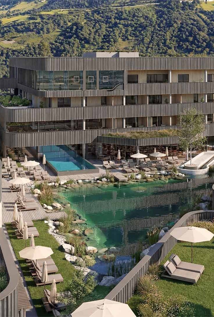 Mehrstöckiges modernes Hotelgebäude mit Holzfassade vor bewaldeten Berg und einem natürlichen Schwimmteich mit Liegestühlen und Sonnenschirmen auf einer Wiese