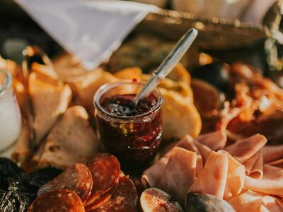 Brett mit verschiedenen Wurst- und Käsesorten, Feigen und einem Glas mit Marmelade und Löffel
