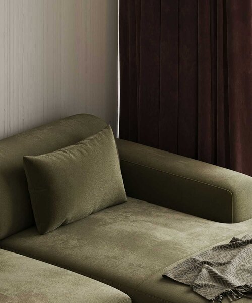 Nahaufnahme eines grünen Sofas mit Kissen und einer Decke vor einer hellen Wand und dunklen Vorhängen