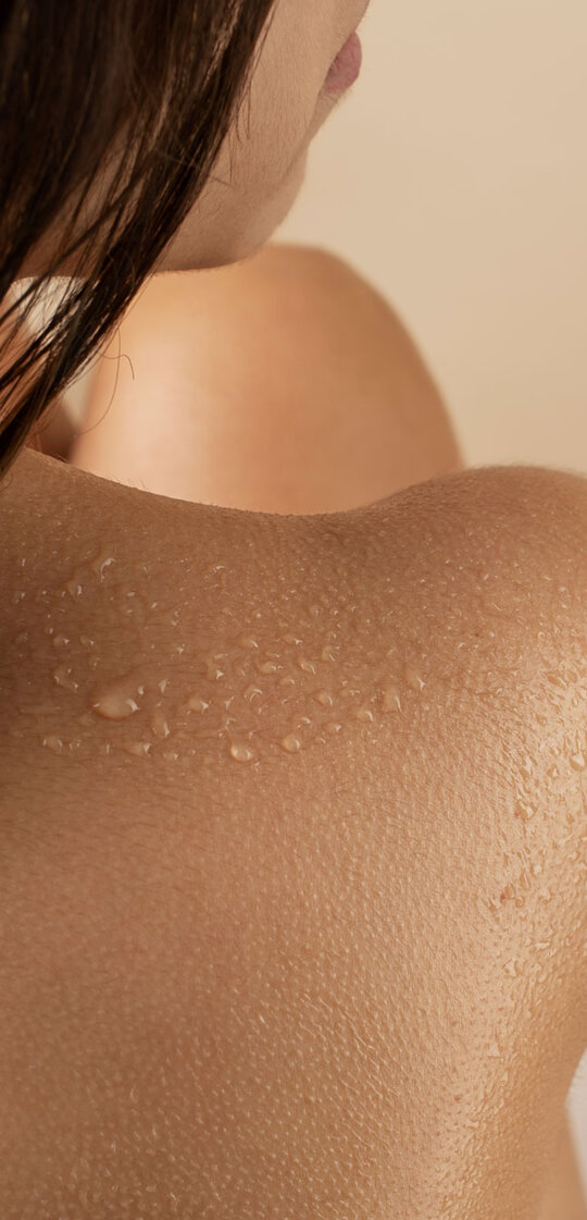Nahaufnahme einer weiblichen Schulter mit Wassertropfen und seitlich sichtbarem Haar