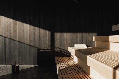 Innenraum einer Sauna mit Holzbänken und Holzwänden, beleuchtet durch Sonnenlicht mit Schattenwurf