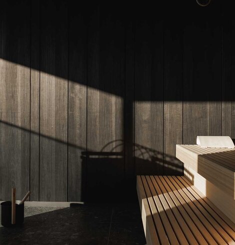 Innenraum einer Sauna mit Holzbänken und Holzwänden, beleuchtet durch Sonnenlicht mit Schattenwurf