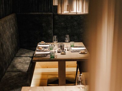 Gedeckter Esstisch mit Gläsern, Tellern und Besteck an einer gepolsterten Sitzbank in einem Restaurant