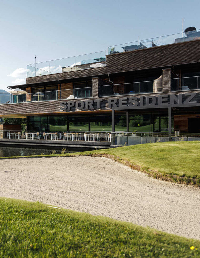 Sportresidenz in seitlicher Ansicht mit See im Vordergrund und Bergen im Hintergrund