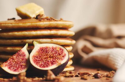 Nahaufnahme eines Stapels Pfannkuchen mit Butter obenauf und zwei halbierten Feigen davor