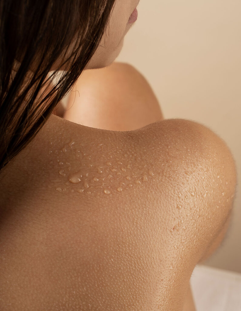 Nahaufnahme einer weiblichen Schulter mit Wassertropfen und seitlich sichtbarem Haar