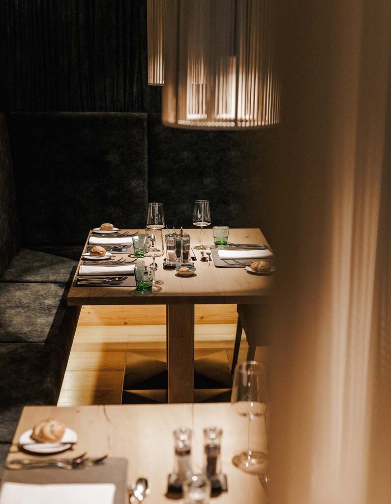 Gedeckter Esstisch mit Gläsern, Tellern und Besteck an einer gepolsterten Sitzbank in einem Restaurant