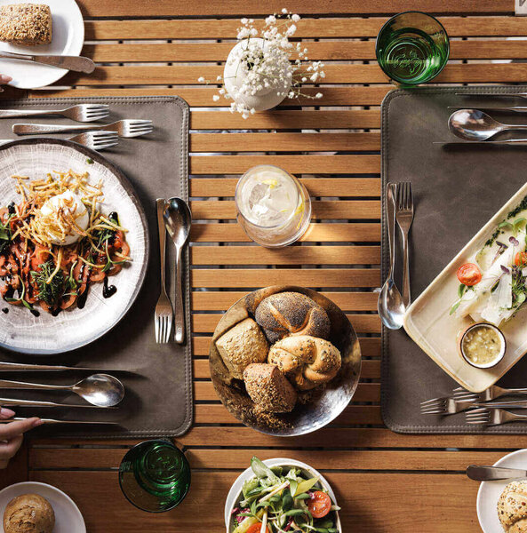 Von oben auf einen Tisch mit zwei Tabletts mit Tellern, Besteck, Gläsern und Brotkörben mit Brötchen und Salat geschaut