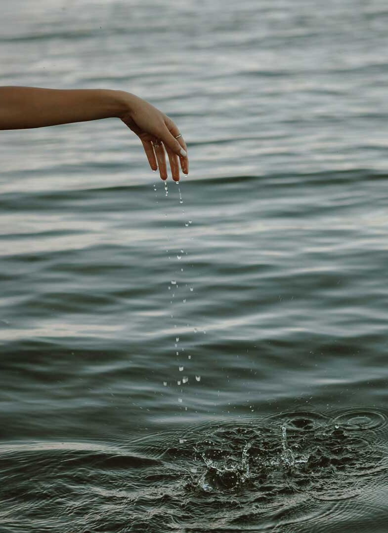 Ausgestreckter Arm über Wasseroberfläche mit fallenden Wassertropfen