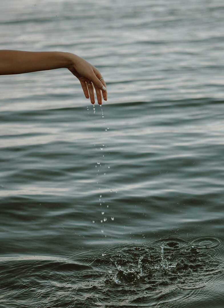 Ausgestreckter Arm über Wasseroberfläche mit fallenden Wassertropfen