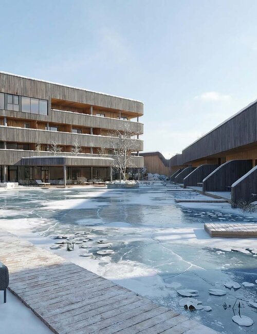 Moderner Gebäudekomplex mit Holzfassaden und gefrorenem Teich im Vordergrund bei winterlicher Landschaft