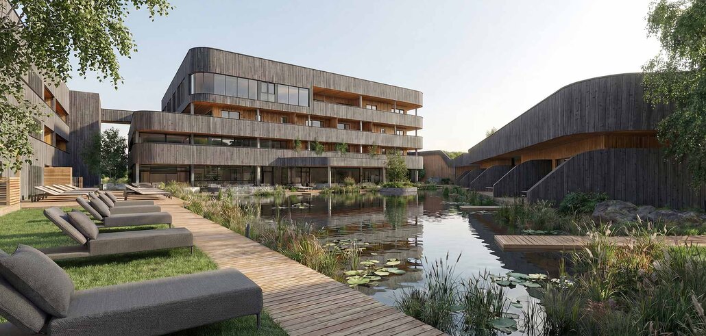 Moderner Gebäudekomplex mit Holzfassaden neben einem Teich mit Seerosen und einem Holzsteg mit Liegen