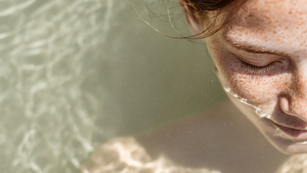Nahaufnahme einer lächelnden Frau mit Sommersprossen und nassen Haaren im Wasser