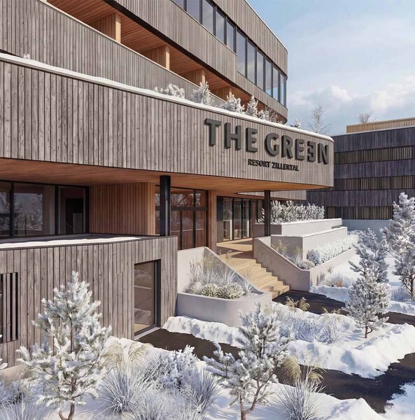 Holzfassade eines modernen Gebäudes mit dem Schriftzug 'THE GREEN' und schneebedeckten Bäumen und Wegen im Vordergrund