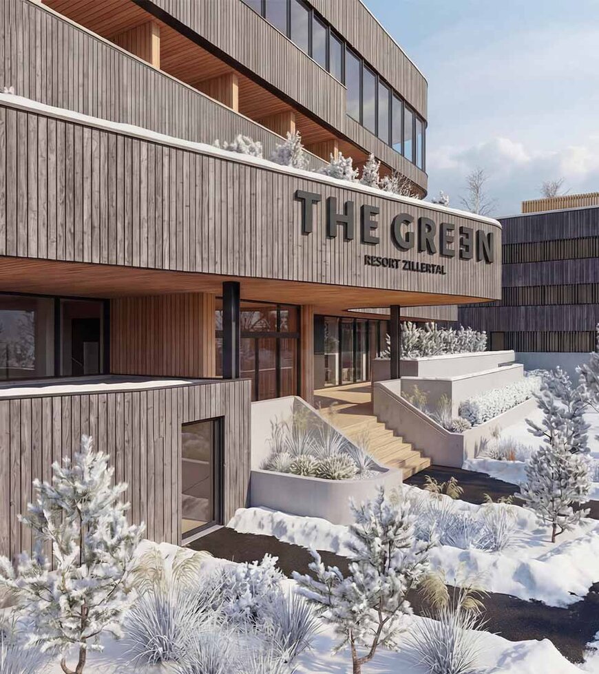 Holzfassade eines modernen Gebäudes mit dem Schriftzug 'THE GREEN' und schneebedeckten Bäumen und Wegen im Vordergrund