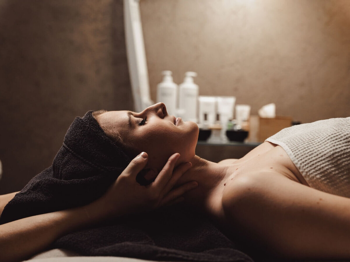 Frau liegt entspannt auf Massagetisch, während Hände ihren Kopf sanft stützen