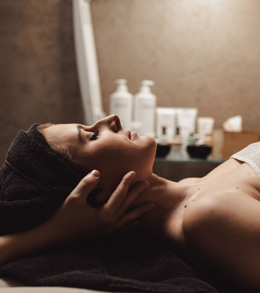 Frau liegt entspannt auf Massagetisch, während Hände ihren Kopf sanft stützen