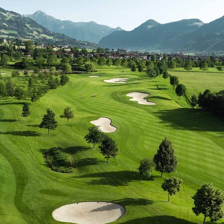 Landschaft mit Golfplatz, Teich, Bäumen und Bergen im Hintergrund
