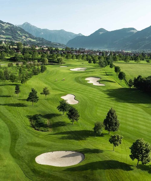 Landschaft mit Golfplatz, Teich, Bäumen und Bergen im Hintergrund