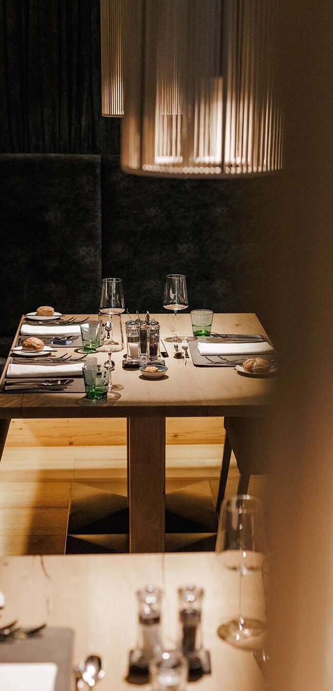 Gedeckter Esstisch mit Gläsern, Tellern und Besteck an einer gepolsterten Sitzbank in einem Restaurant
