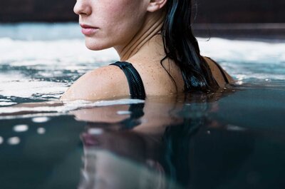 Frau mit nassem schwarzen Badeanzug steht im Wasser und blickt seitlich weg