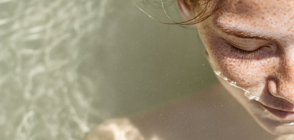 Nahaufnahme einer lächelnden Frau mit Sommersprossen und nassen Haaren im Wasser