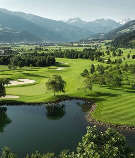 Landschaft mit Golfplatz, Teich, Bäumen und Bergen im Hintergrund