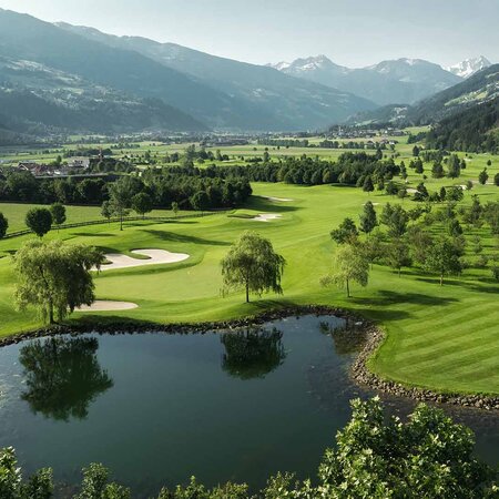 Landschaft mit Golfplatz, Teich, Bäumen und Bergen im Hintergrund
