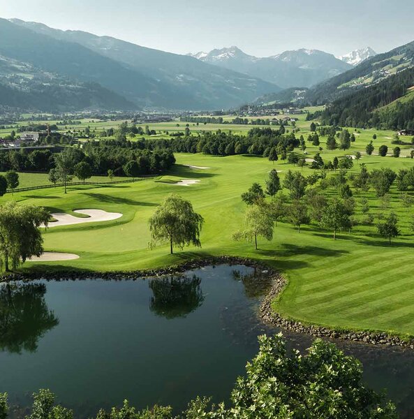 Landschaft mit Golfplatz, Teich, Bäumen und Bergen im Hintergrund