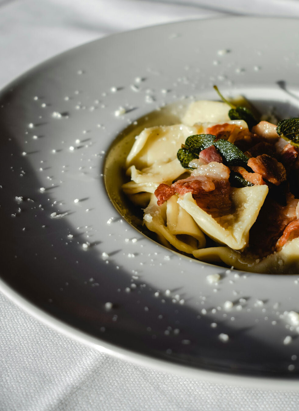 Nahaufnahme eines weißen Tellers mit Pasta, Speckstücken und Salbeiblättern