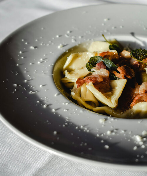 Nahaufnahme eines weißen Tellers mit Pasta, Speckstücken und Salbeiblättern