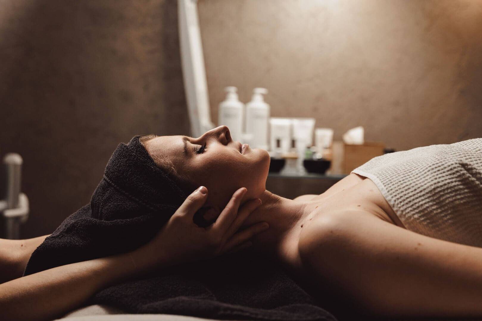 Frau liegt entspannt auf Massagetisch, während Hände ihren Kopf sanft stützen